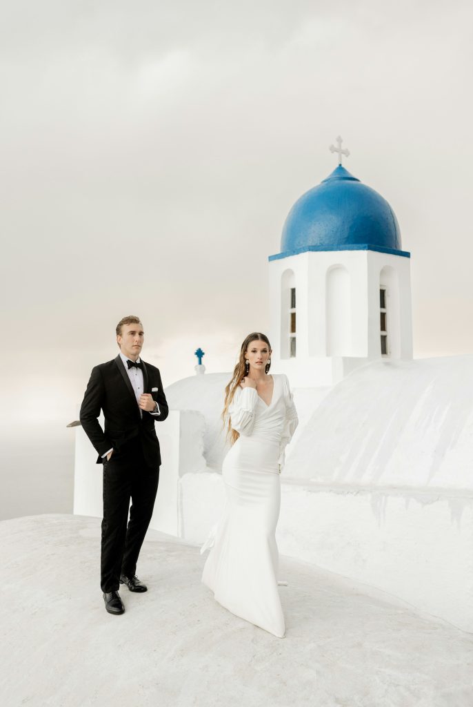 A bride and groom beside a blue-domed Greek chapel